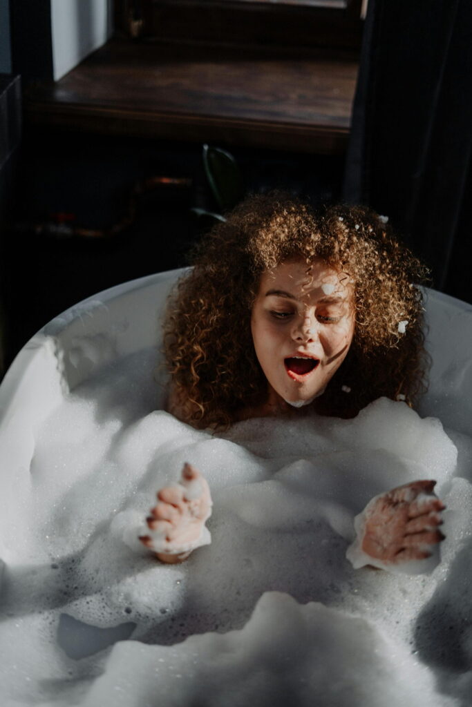 A woman enjoys a bubble bath with an open smile on her face