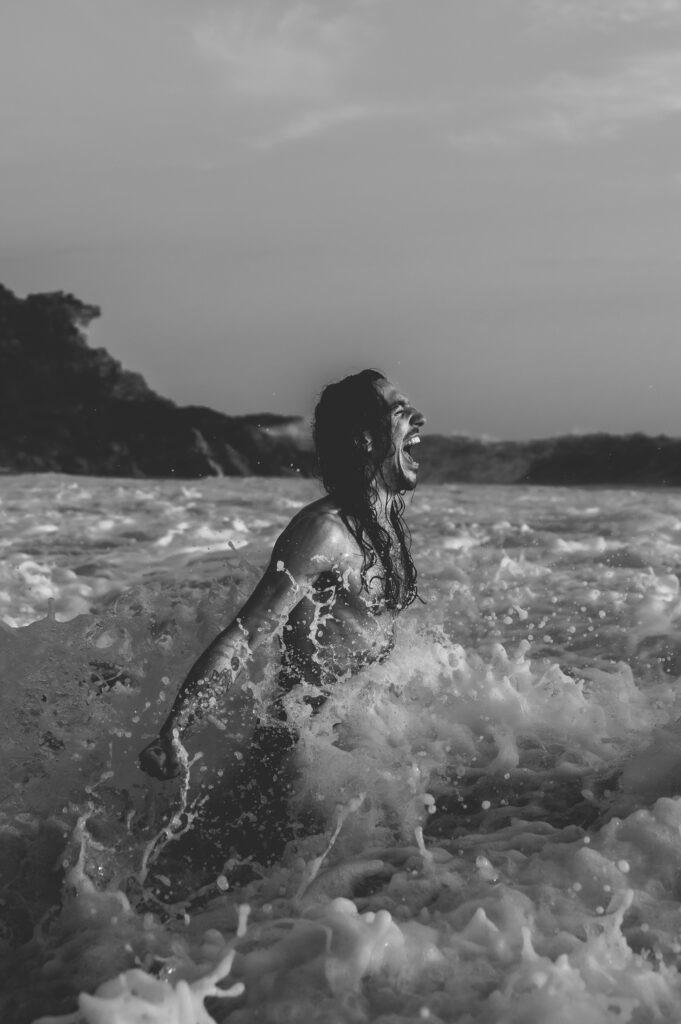 A person standing in a breaking wave—symbolizing letting go, renewal, and embodied change