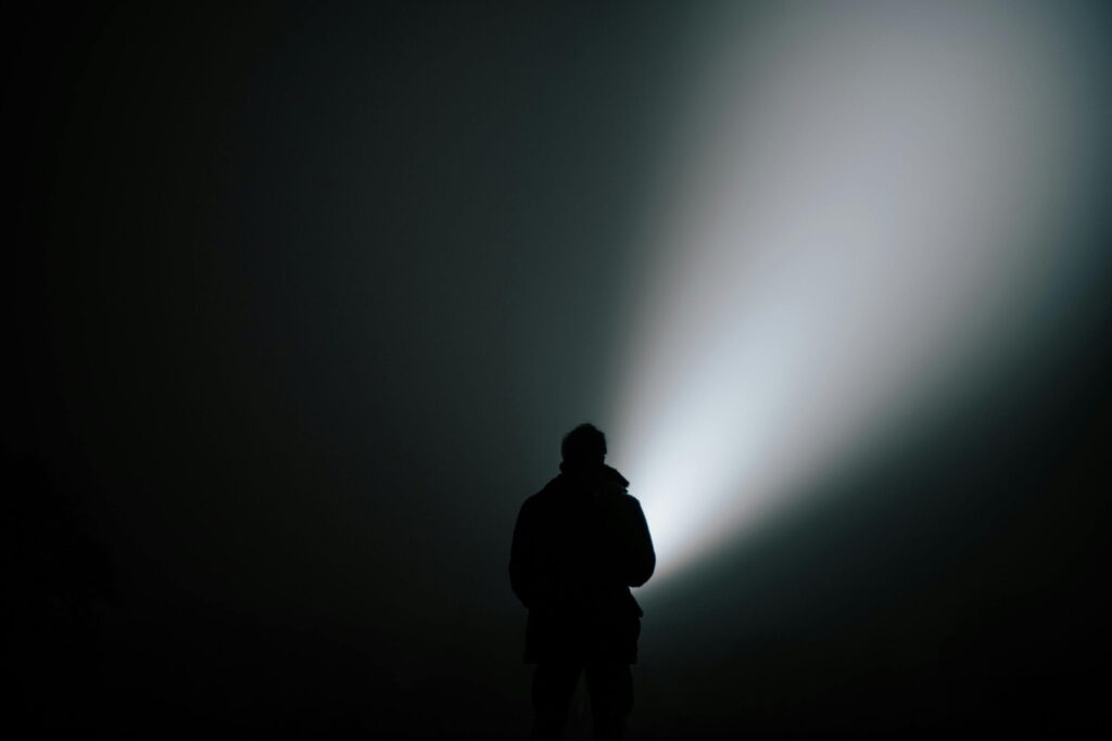 Ein Mensch mit Taschenlampe in völliger Dunkelheit – Symbol für Orientierung, Präsenz und innere Führung im somatischen Coaching