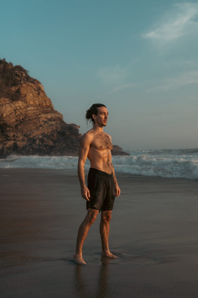 Nico Loewer steht selbstbewusst am Strand im Sonnenlicht mit Blick aufs Meer