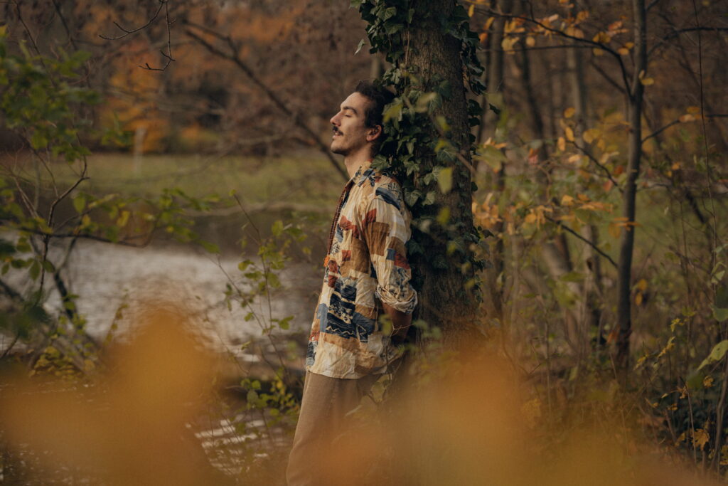 man leaning on a tree surrounded by ivy looking relaxed