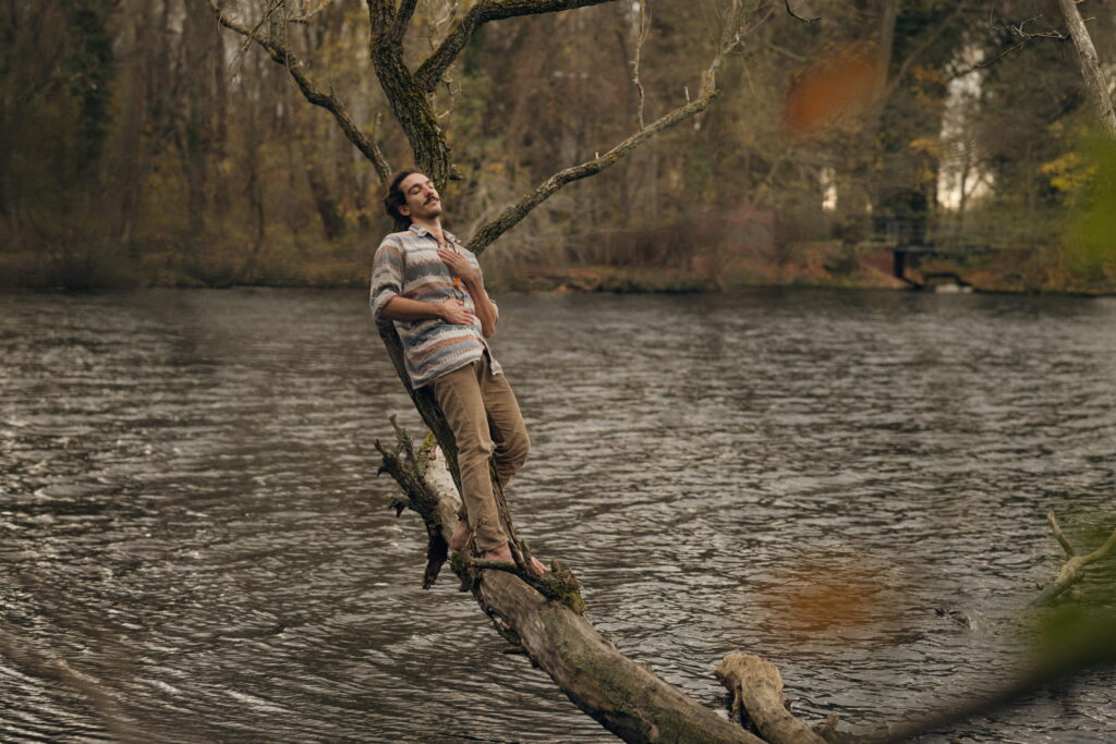 nico leaning on a branch over the water holding his hear with eyes closed