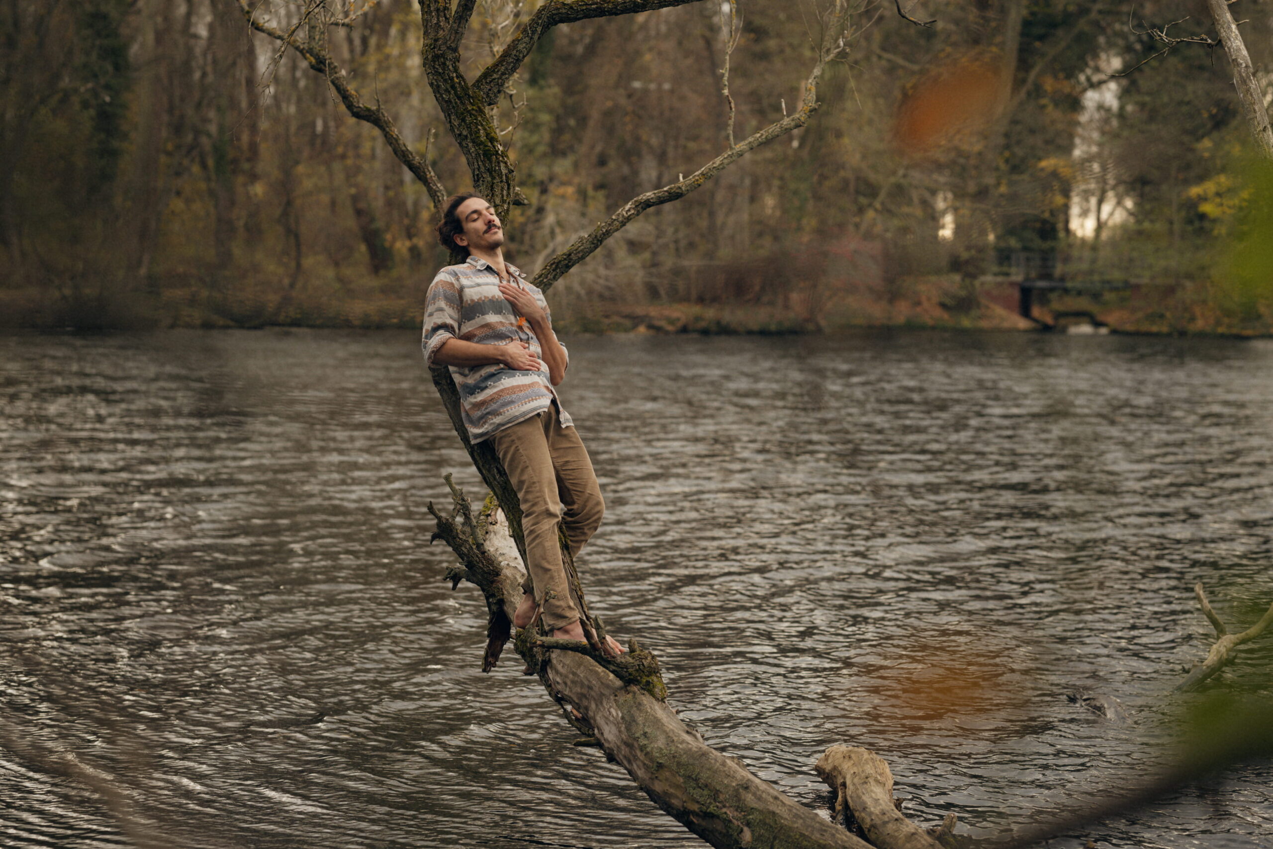 nico leaning on a branch over the water holding his hear with eyes closed