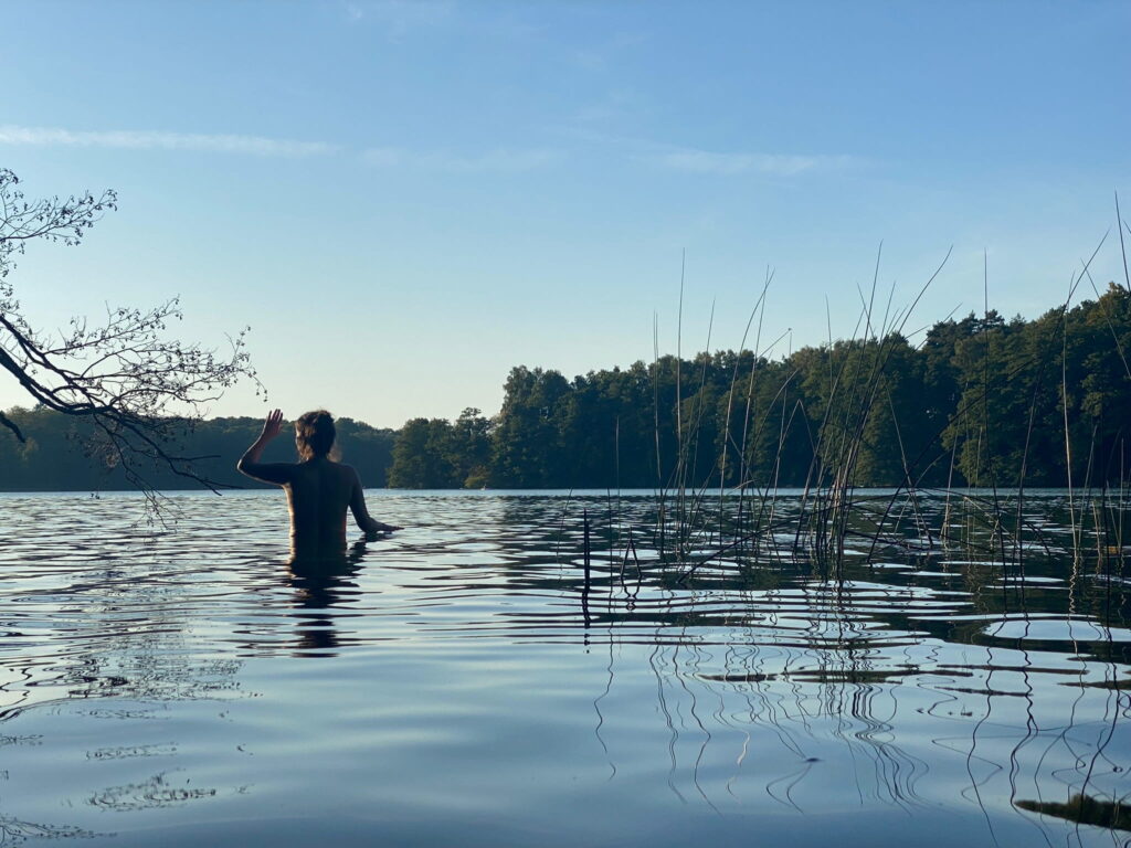 Frau steht im Wasser und blickt in die Sonne als Symbol für Lebendigkeit, Selbstvertrauen und bewusste Präsenz im Körper