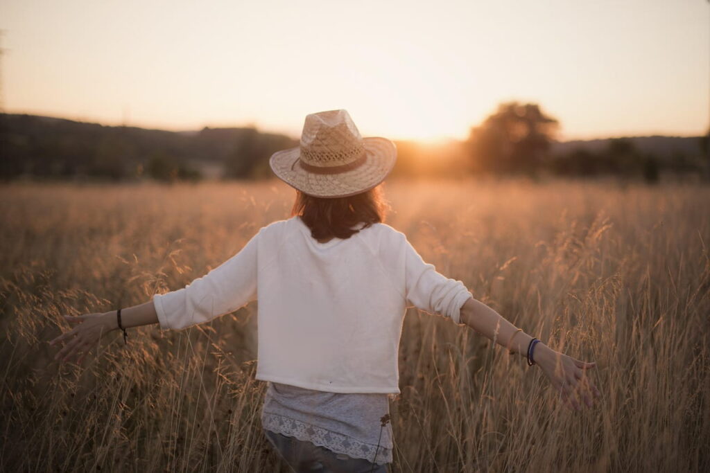 Woman walking through a field of tall grass, stretching in warm light