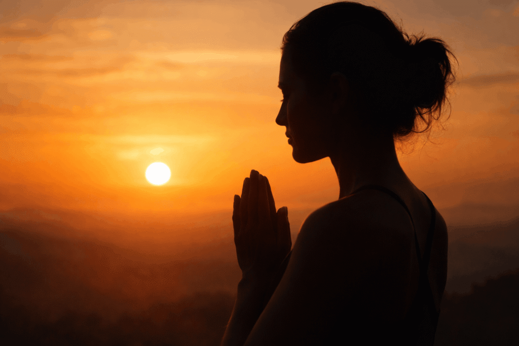 eine frau bei sonnenaufgang mit gebetshänden