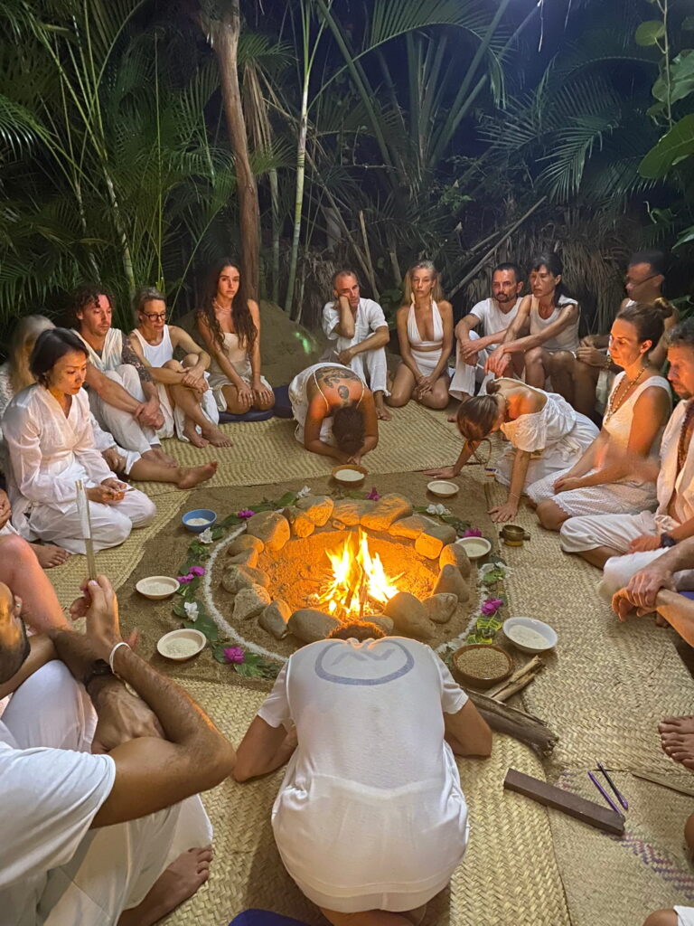 Teilnehmende in weißer Kleidung sitzen im Kreis um ein Feuer während eines Tantra Rituals im Workshop-Kontext