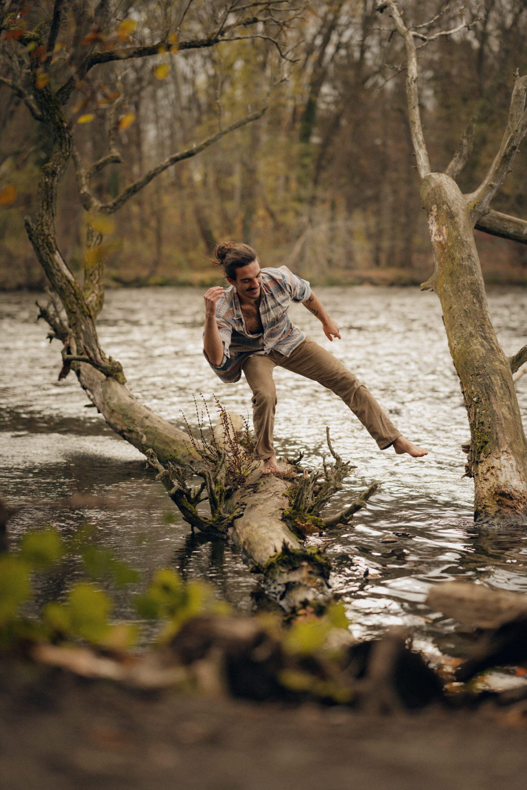 Nico Loewer smiling as he balances on a tree trunk above the water—a symbol of balance, presence, and embodied stability