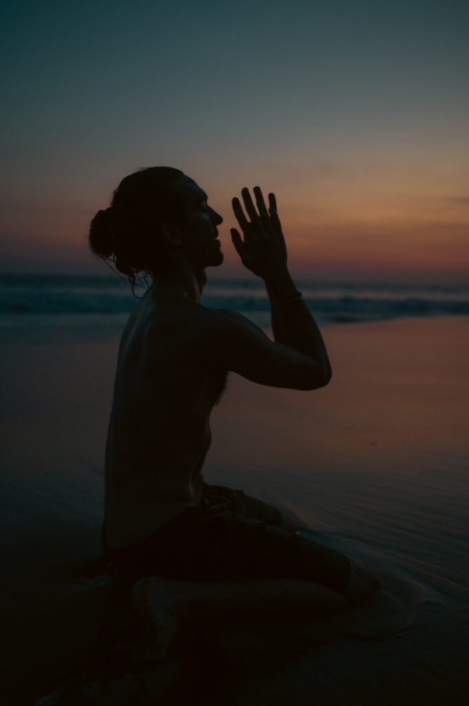 man is sitting in prayer while sunset in background