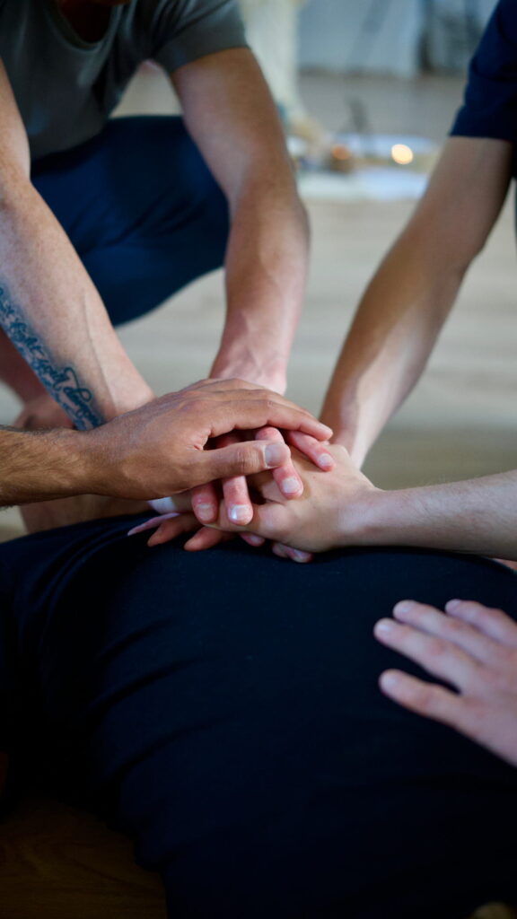 Mindful hands of men resting on a participant’s chest during a men’s work process—symbolizing support and co-regulation